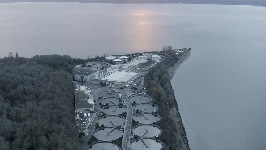 Pullback tilt up reveal of a large wastewater treatment facility situated along an ocean bay