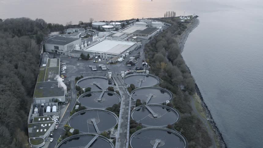 Tilt up reveal of calm coastal water surrounding a sewage treatment plant at sunset