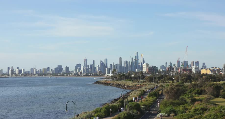 People walking near the ocean in a park close to a city skyline