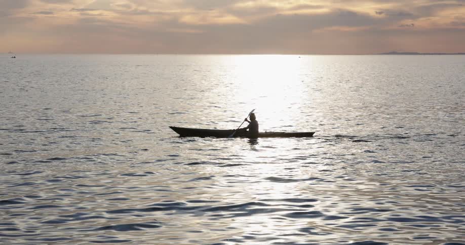 The silhouette of a person paddling a boat at dawn