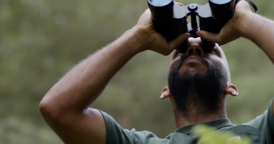 A bearded man looking through binoculars in the forest