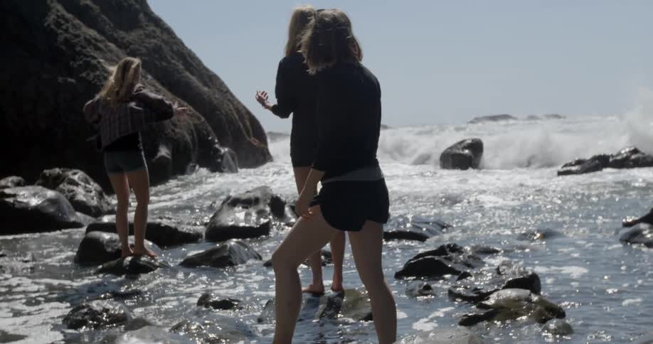 Three women carefully walking on rocks on the shore