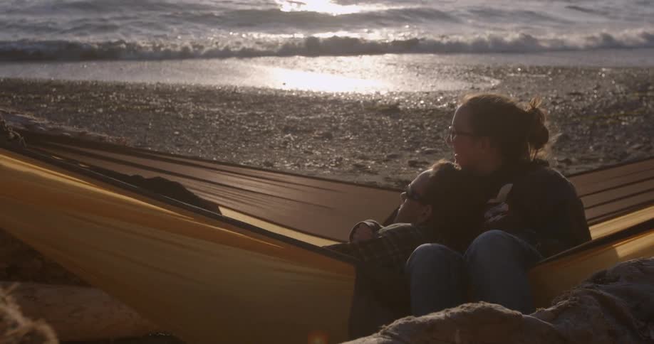 Two people are lying in a hammock on the beach