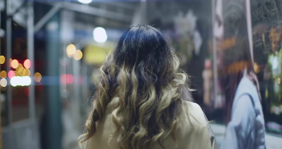 A woman with long curly hair walking on a city sidewalk at night