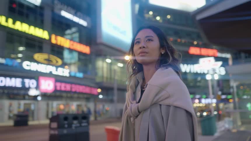A woman standing on a city street with vehicles and buildings in the background