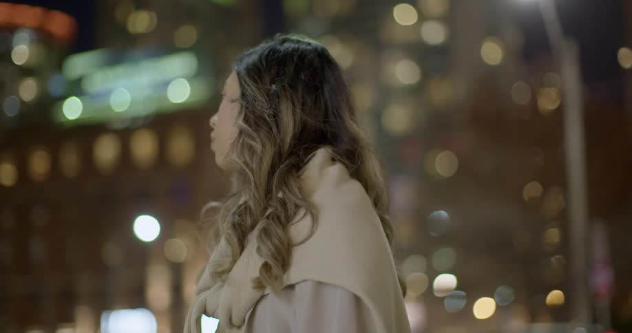 A woman stands on a city street at night looking at all the shimmering glowing lights