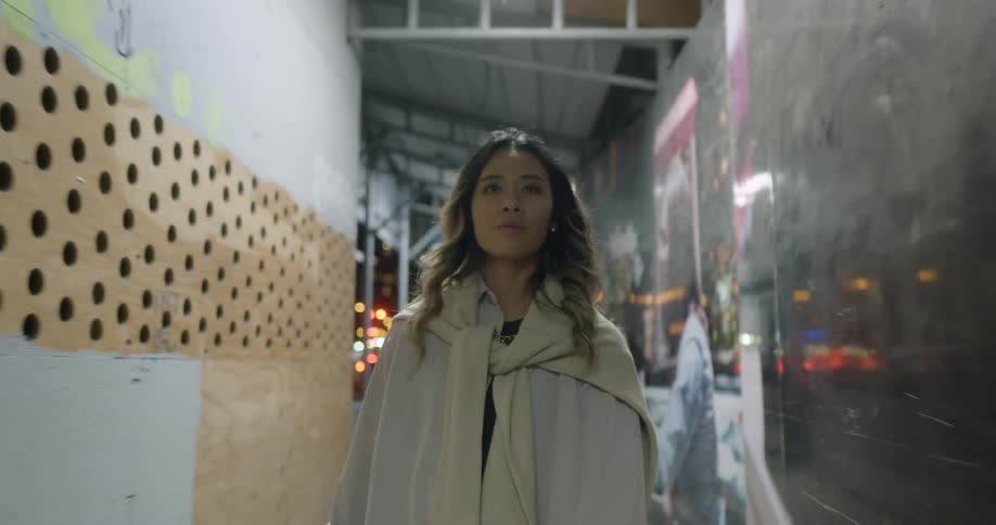 Young woman with a sweater on her shoulders walking on a hallway at night