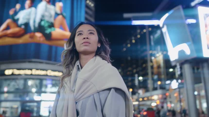 A woman stands on a street in a downtown area with many buildings lights and signs