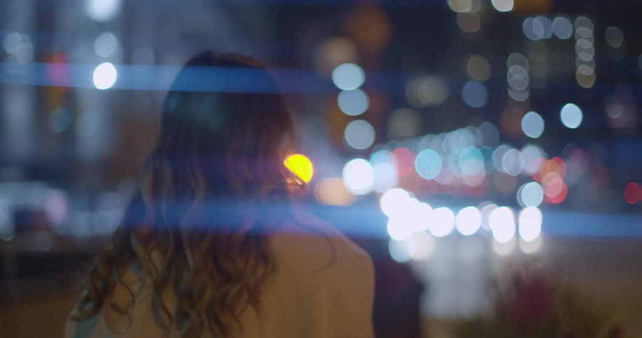 A woman walks on a city sidewalk at night