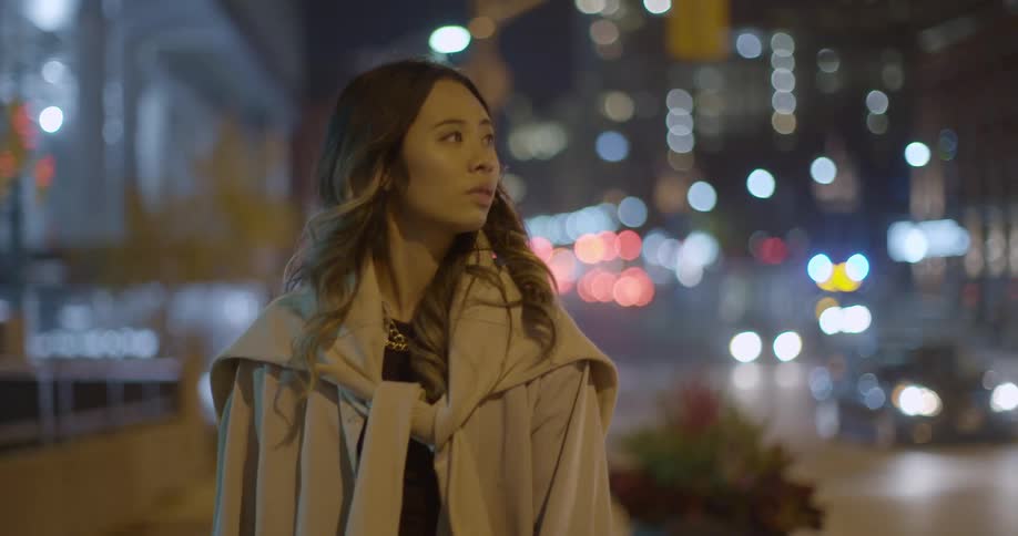 A woman walks on a sidewalk of a city area at night