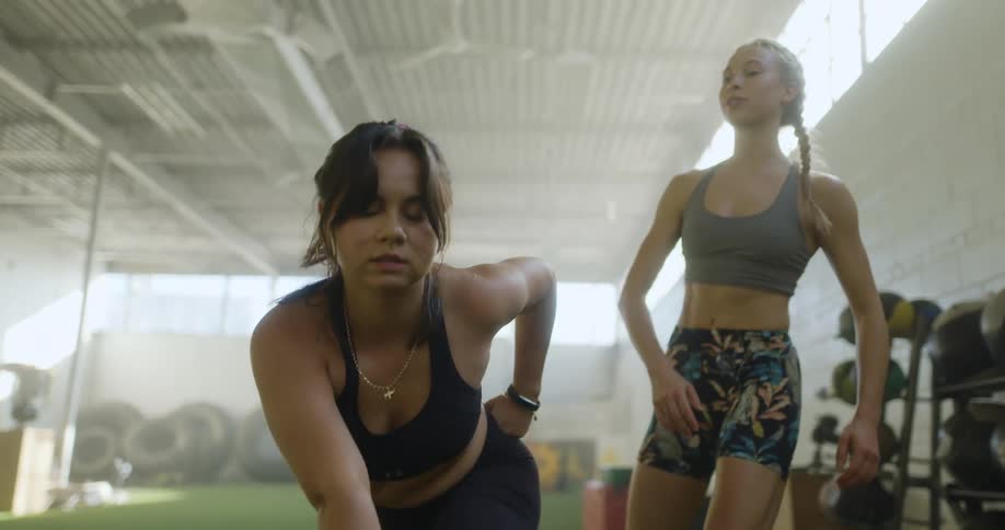 A personal trainer helps a woman stretch forward and down in a field house