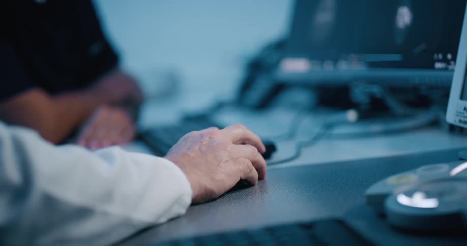Two men sit at a desk moving a computer mouse with one hand