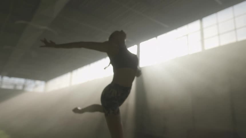 A woman leaps in the air while indoors with sun streaming through the windows