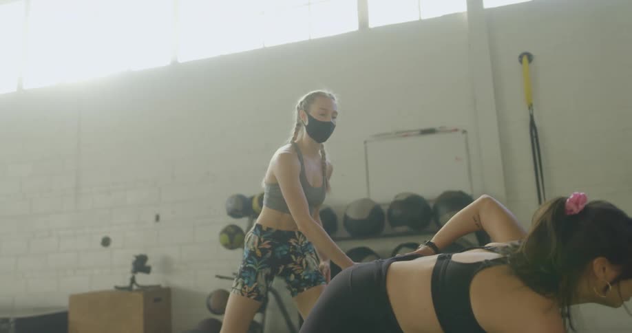 A woman does stretches in a gymnasium as a personal trainer watches her