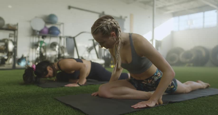 Two women stretching on mats with exercise equipment in the background