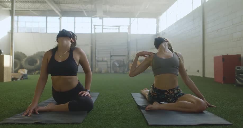 Two women are stretching indoors during the day
