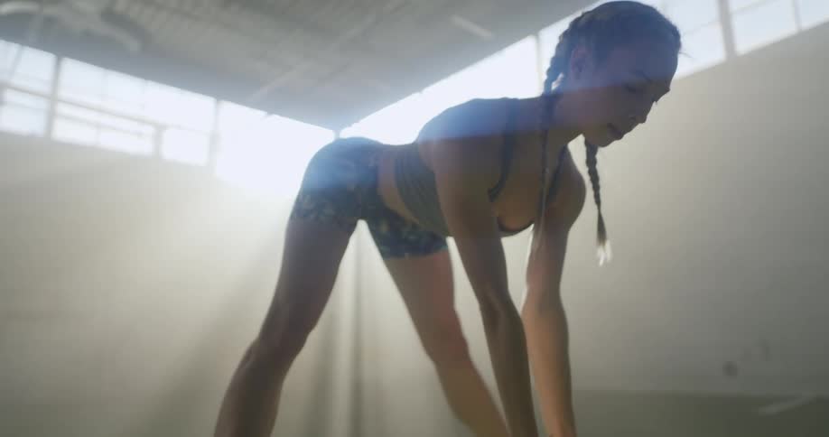 A woman in a sports bra and exercise shorts stretching in a sunny fitness room