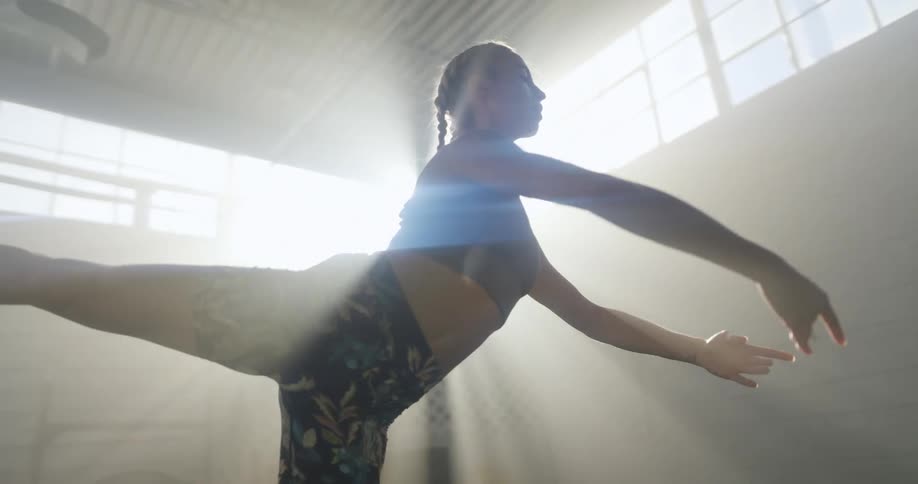 A thin and muscular woman performs a stretching exercise indoors in a gym