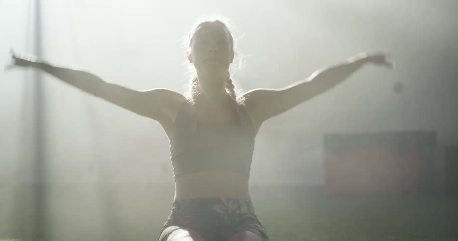 A woman stretches on the turf in a gym while steam billows behind her