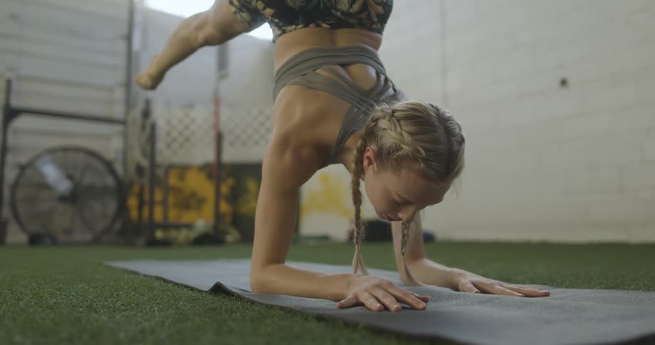 A blonde woman balancing on her arms on a yoga mat in a fitness room