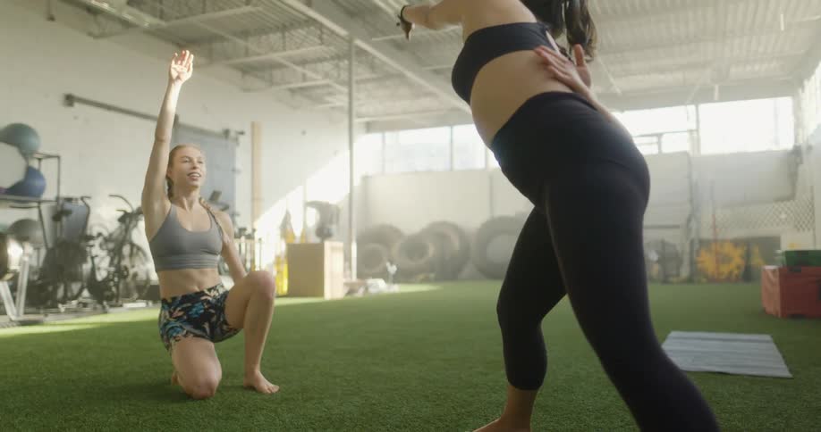 Two women in a room stretching with exercise equipment in the background