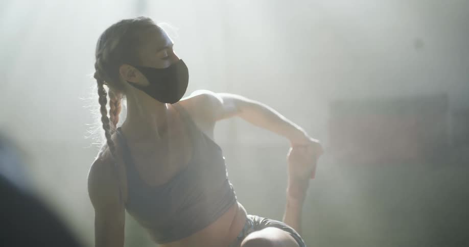 A woman in a room with a mask stretching with a wall in the background