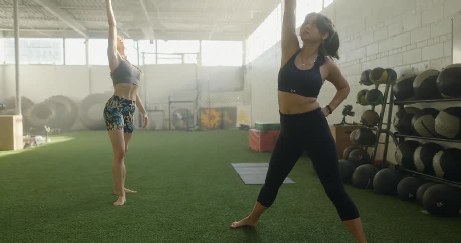 Two women in sports bras stretching in a fitness room