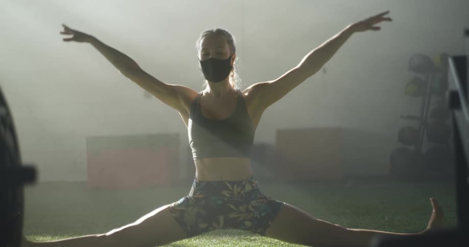 A woman in a straddle split in the grass lifts herself up and raises her arms above her head