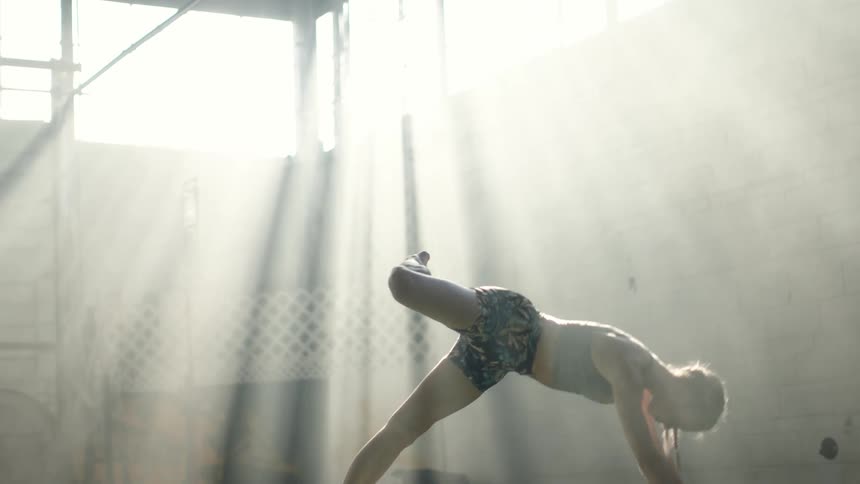 Morning sunlight over a young fit woman wearing sports clothes stretching on the floor of a gym
