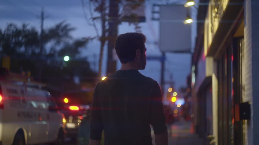 A man walks along a small town sidewalk beside buildings at night