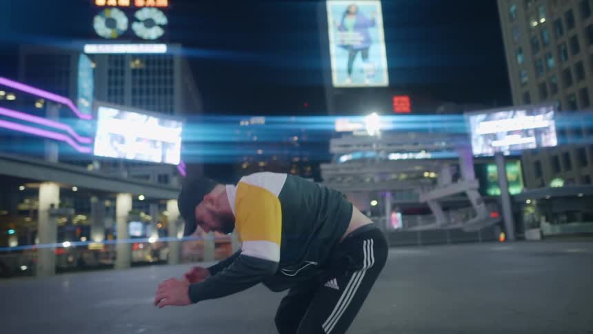 A man performs a back flip in the middle of a plaza surrounded by tall buildings