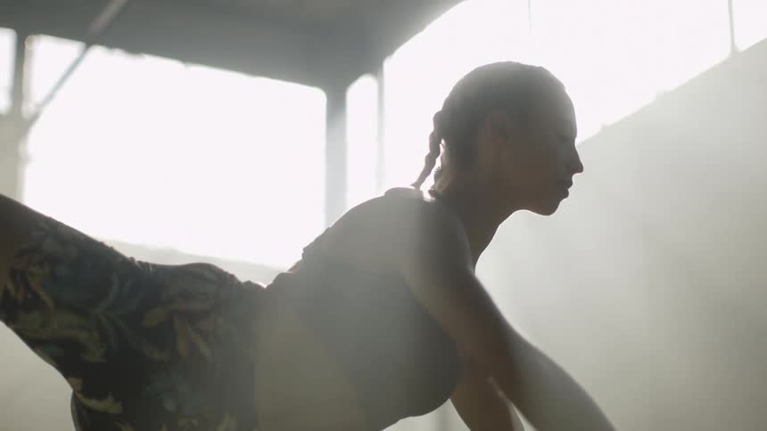 A woman stretches her back leg up in a ballet style pose while working out