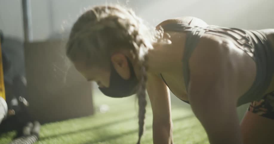 Young fit woman wearing a face mask and sports clothes stretching on the floor of a gym at morning