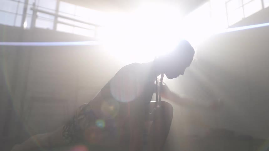 Sunlight filters through the window of a gym over a young fit woman wearing sports clothes stretching in yoga poses