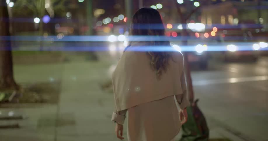 A woman walks alone on a city sidewalk with vehicles passing by