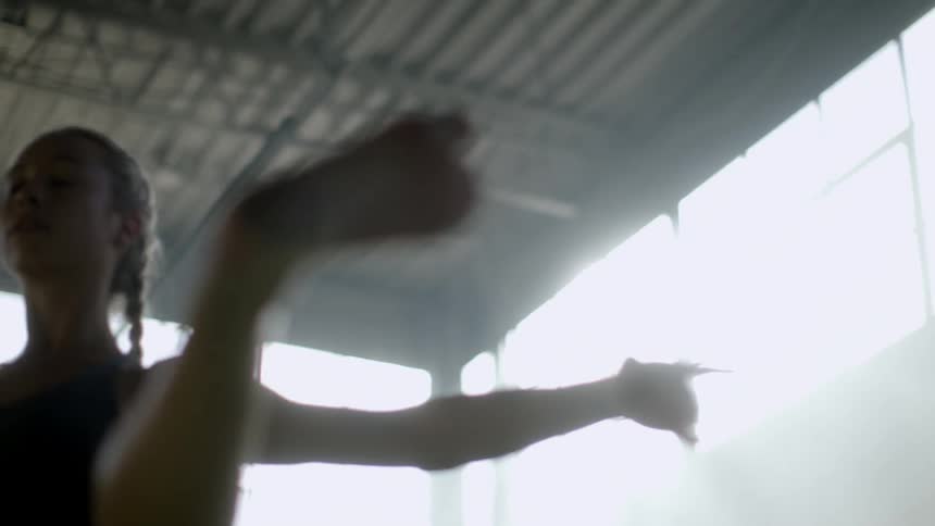 A woman stretches her legs and arms while indoors with sun streaming through windows