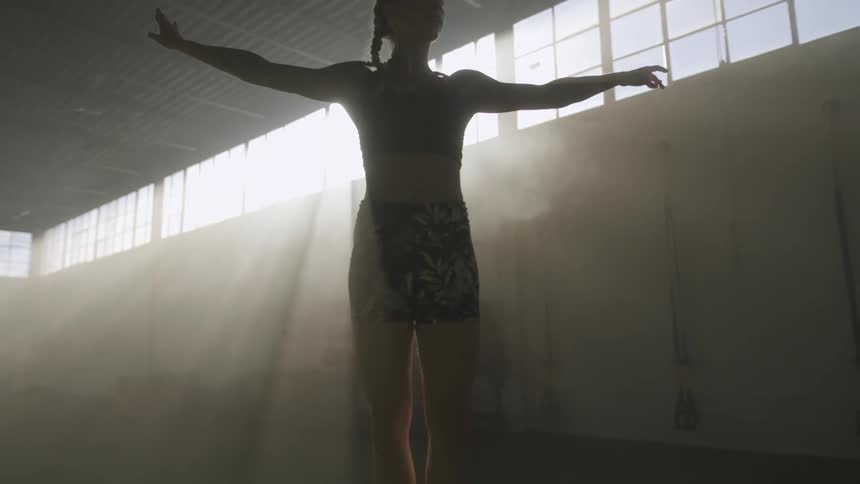 A female dancer performs a graceful leap in a dimly lit building during the day