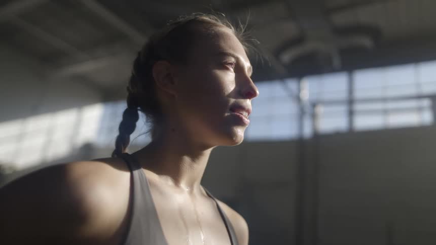 A woman with sweat running down her chest stands in a building
