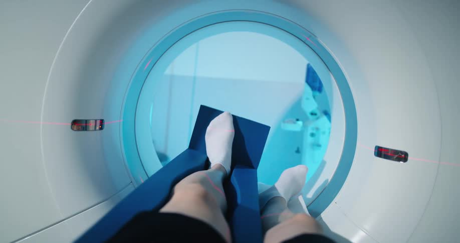 A patient lying on the table of an mri machine with one leg in a brace is slowly carried through the scanner
