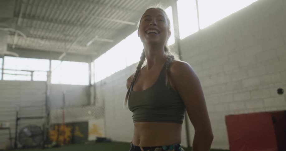 A woman in a sports bra smiling and laughing while standing in a fitness room