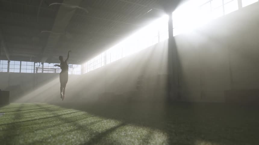 A woman does ballet jumps while working out inside a field house