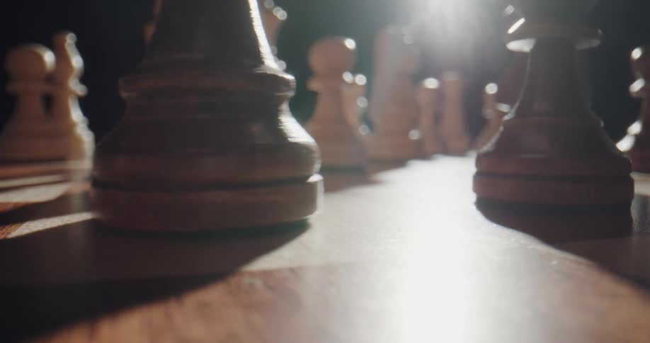 A chess piece slides across the wooden board as a light glares against black