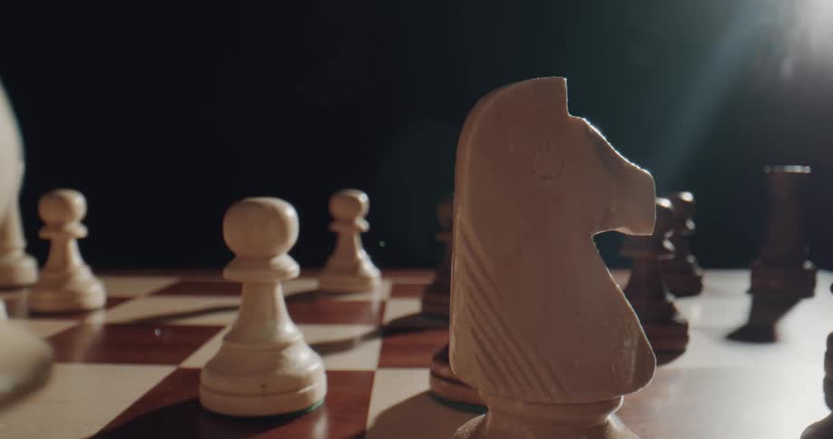 Close up of players placing chess pieces over a chessboard in a dark room