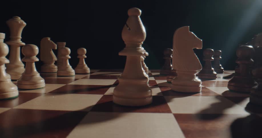 A close up of a chess board with hands moving chess pieces on the board