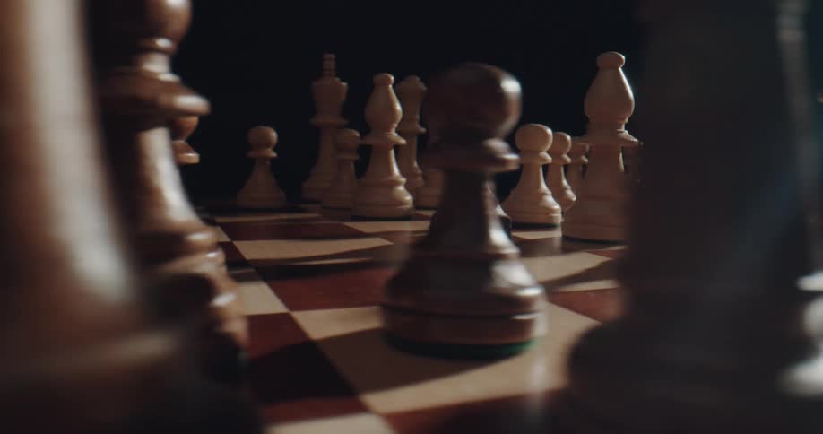 Chessboard with chess pieces spinning under a spotlight in a dark room