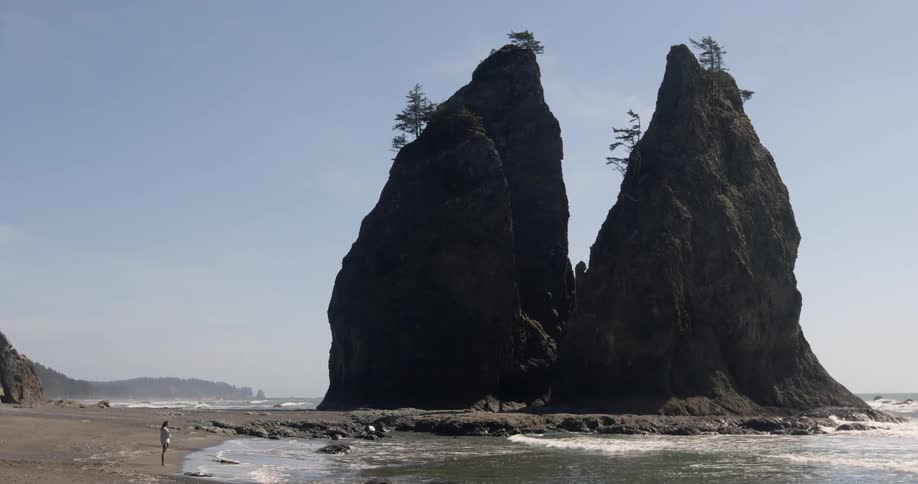 A person stands by the shore with two rocks nearby