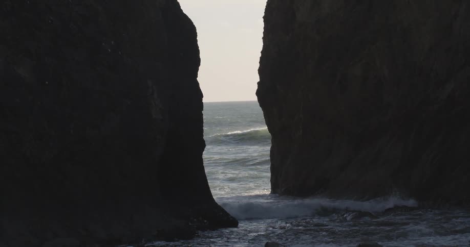 Water is crashing on two large rocks in the shore