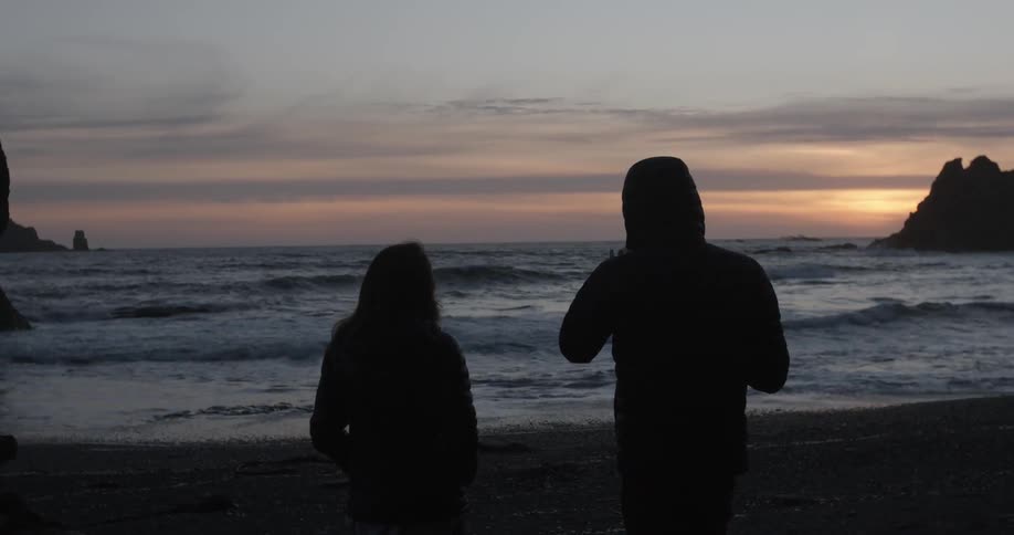 Two people are standing on a beach at dawn