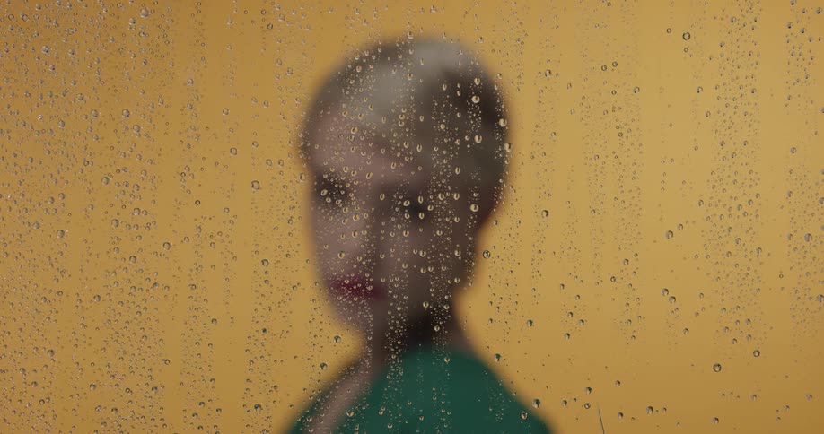 Young blonde short haired woman looking at the camera behind a wet glass