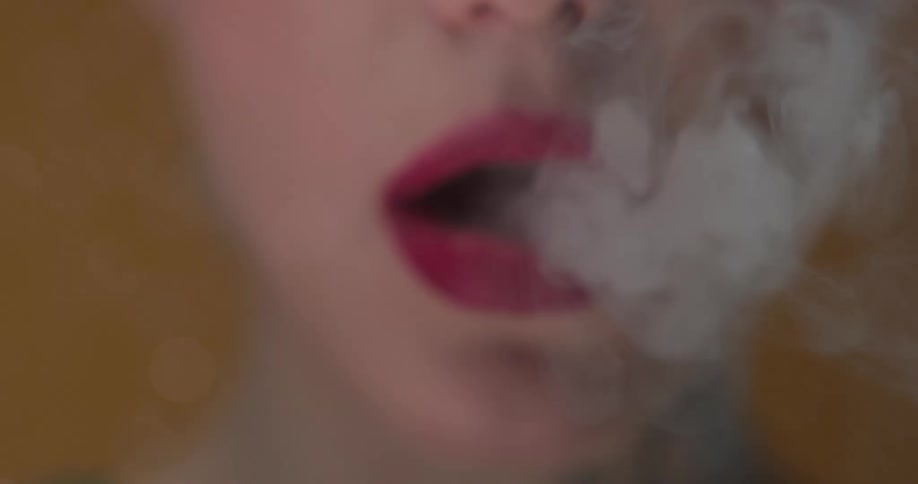 Close up of a woman smoking a cigarette and exhaling the smoke through the red lips of her mouth